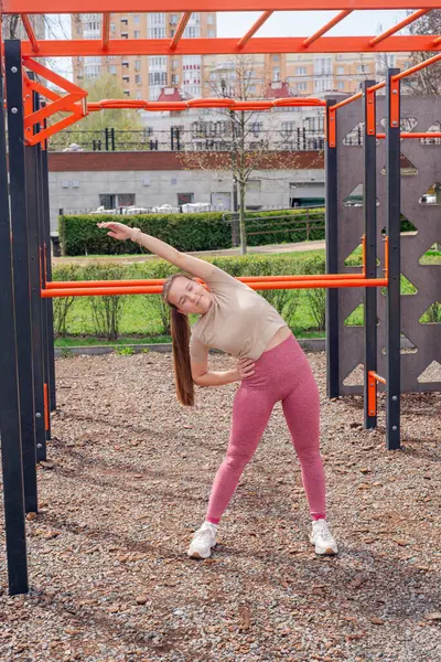 Genç bir kadın spor salonunda bacak ve kol hareketleri yapıyor, spor kıyafetler giyiyor, bahar havasında aktif ve sağlıklı kalıyor..