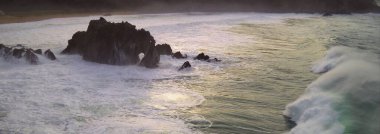 Vista panormica de las olas del ocano rompiendo en las rocas al atardecer clipart