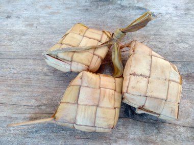 Tahta arka planda Tipat / Ketupat (Rice Dumpling). Ketupat, Bayram Bayramında, İdul Fitri / Aidilfitri 'de pilav pişirmek için genç hindistan cevizi yapraklarından yapılan doğal pirinç kabı.