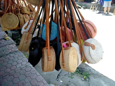 Bir sokak dükkanında hatıra olarak asılı duran ikonik rattan el çantaları. Sokak dükkanında Rattan marka yuvarlak çantalar. Bali, Endonezya 'da yerel bir hediyelik eşya pazarında ünlü Balili rattan eko çantaları. ( Tas Anyaman )