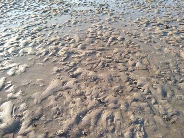 Sahilde gelgit var. Sahilde kum, arka plan olarak. Güneşli bir günde güzel kumsal dokusu. Yazın kumsaldaki kum desenlerinin arka planı ve dokusu