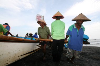 Balıkçılar tekneleri kıyıya taşımak ve itmek için birlikte çalışıyorlar.