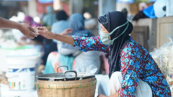 Yüzünde maske olan yaşlı bir kadın mallarını Bantul, Yogyakarta 'daki Niten Market' te satıyor.