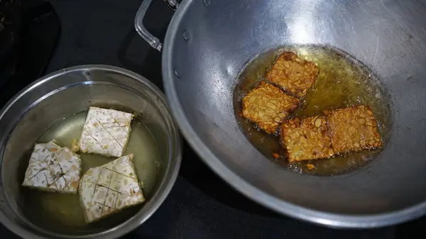 stock image Tempeh or tempe that is being fried in a frying pan and tempeh that has not been fried. Focus selected