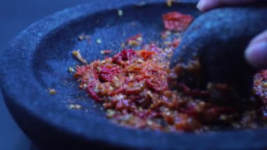 El, kırmızı biber sosunu taştan bir havanda öğütüyor. Şef geleneksel Endonezya baharatlı acı biber sosu hazırlıyor.