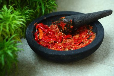 Kırmızı biber sosu, taş bir harç ve tokmak üzerinde. Yanında yeşillik var.