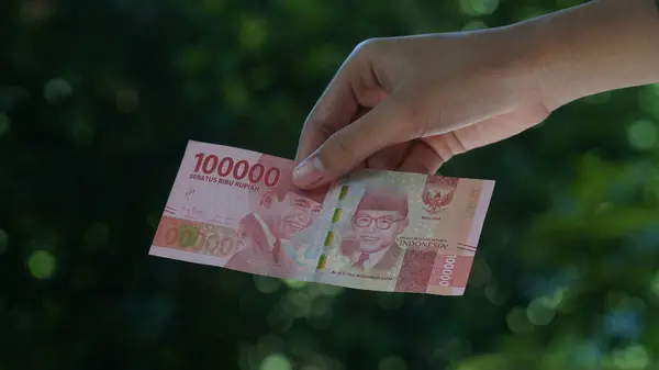 stock image The Indonesian currency, the 100,000 rupiah note, is held in a woman's hand. Focus selected