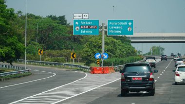 Trans Java toll road at noon. There are signs for the city of Pandaan, Lawang, Malang, Taman Safari clipart