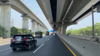 Jakarta 'da otoyolda giden araçlar var. Yükseltilmiş bir paralı yol ve üzerinde bir demiryolu hattı var.