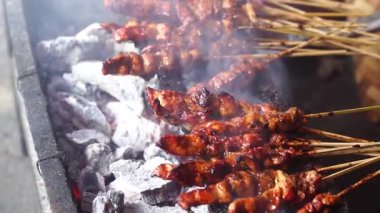 Tavuk satay mangal kömürü üzerinde kızartılıyor, ince duman yükseliyor. Seçilene odaklan