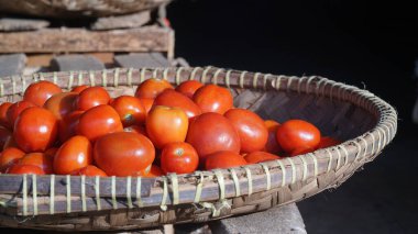 Bambu sepetinde güneş ışığına maruz kalmış bir yığın kırmızı domates. Seçilene odaklan