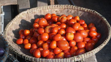 Bambu sepetinde güneş ışığına maruz kalmış bir yığın kırmızı domates. Seçilene odaklan