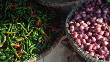 Shallotlar veya kırmızı soğanlar ve bambu sepetlerindeki yeşil biberler, sabah güneşine maruz kalıyorlar. Seçilene odaklan