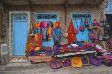 Fas yapımı el işleri, halılar, elbiseler, çantalar ve diğer ürünler Fas 'ın mavi kenti Chefchaouen Medina' nın sokaklarında duvarda asılı duruyor. Satılık çeşitli eşyalar..