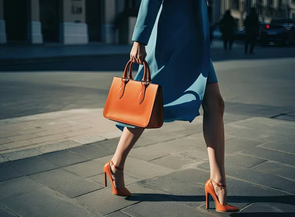Women\'s legs in orange shoes. Bright orange shoes and handbag. Stylish slim girl in soft blue warm coat, gray warm dress and heels walking on the rainy wet street. foto