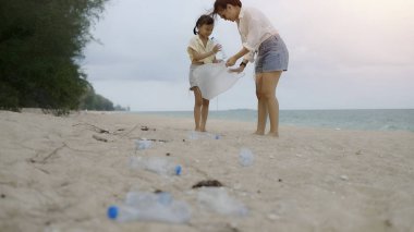 Bir kadın ve bir çocuk sahilde çöp topluyor. Kadın plastik bir çanta tutuyor ve çocuk da bir şişe tutuyor. Sahne, çevreyi temiz tutmanın önemini anlatıyor.