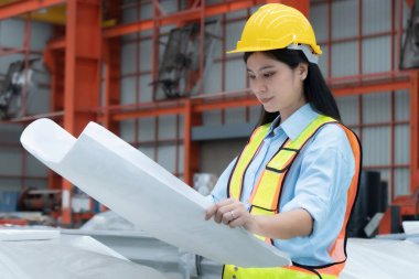 Çalışan kadın mühendis planları elinde tutuyor ve bir bina ve inşaat alanının yapısını inceliyor.