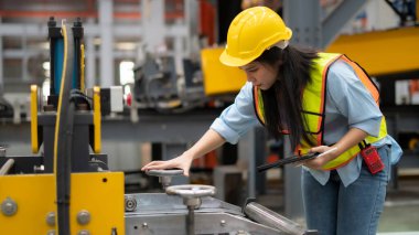 Elinde tablet bulunan kadın mühendis fabrikada makine teftişi yapıyor.