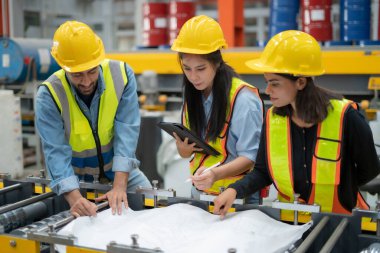 Mühendisler ve yöneticiler bir fabrika salonunda mühendislik çizimlerini tartışıyor. Modern endüstriyel salonda kalite kontrol görevleri prodüksiyon mesleği yapıyor