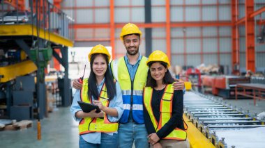 Genç ve gülümseyen genç kadın işçi modern endüstriyel fabrikada ya da fabrikada iş kıyafetleri ve kaskla büyük bir fabrikada duruyor..