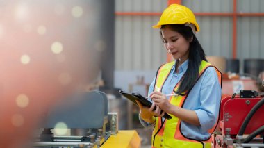 Bir kadın fabrika işçisi üretim sırasında fabrikanın kalitesini kontrol eder. Güvenli kıyafetler giyin Dijital tablet kullanın