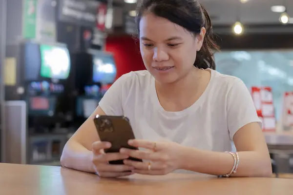 Güzel genç bir kadın akıllı telefondan mesaj göndermek için oturuyor ve cep telefonu kullanıyor.