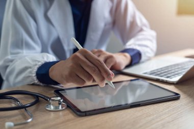 Doktorun muayenehanesindeki tıbbi ve sağlık konseptinde dijital tabletle dizüstü bilgisayarda çalışan doktorların yakın çekimi