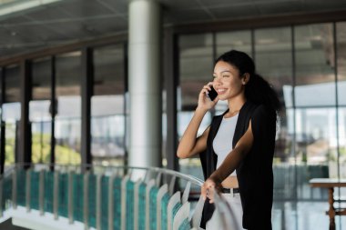 Bir kadın balkonda dururken cep telefonuyla konuşuyor. Gülümsüyor ve sohbetten zevk alıyor.