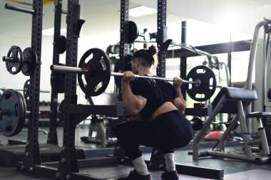 Bir adam spor salonunda ağırlık kaldırıyor. Sahne odaklanmış ve odaklanmış. Adam bir halter kaldırır ve çömelir. Bu da gücünü ve formülünü geliştirmek için çok çalıştığını gösterir..