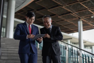 Takım elbiseli iki adam merdivenlerde duruyordu. Elinde bir tabletle önemli konuları tartışıyorlar..