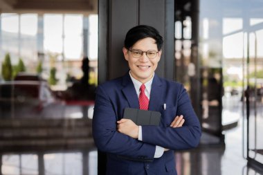 Takım elbiseli ve kravatlı bir adam sağ elinde bir tablet tutuyor. Gülümser, kendinden emin ve profesyoneldir. Modernlik ve teknolojik ilerleme kavramı