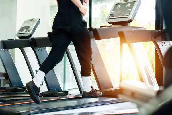 Spor salonunda koşu bandında koşan biri. Siyah pantolon ve beyaz çorap giyiyor.