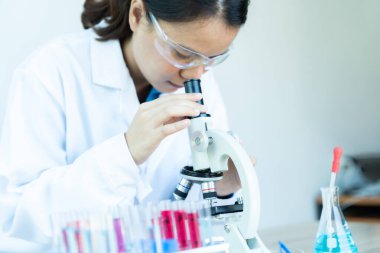 Laboratuvar önlüklü bir kadın mikroskoptan bakıyor. Bilimsel merak ve odaklanma kavramı