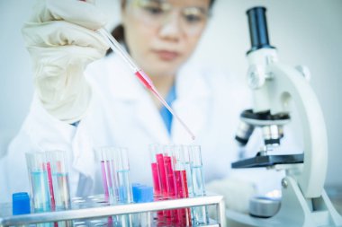 Laboratuvar önlüklü bir kadın kırmızı sıvıyı test tüpüne aktarmak için pipet kullanıyor.