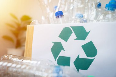 Üzerinde yeşil geri dönüşüm sembolü olan bir kutu. Kutu plastik şişelerle dolu. Geri dönüşüm kavramı ve atıkların azaltılmasının önemi