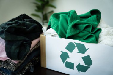 Yeşil geri dönüşüm sembolü olan bir kutunun üstüne bir kutu dolusu kıyafet yığılır. Kıyafetlerin hepsi farklı renkler ve stiller, ve kutu onlarla dolup taşıyor. Giysileri geri dönüşüm ve yeniden kullanma kavramı