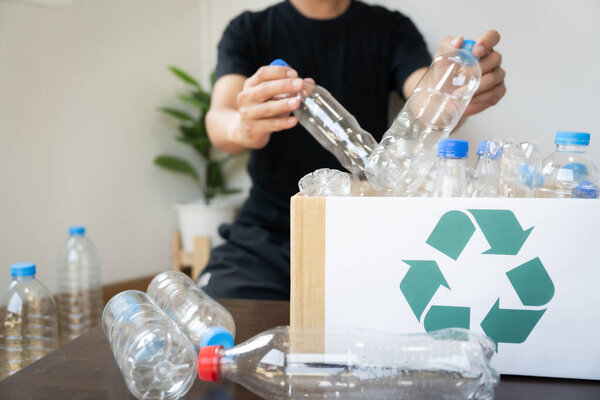 Мужчина держит коробку пластиковых бутылок и символ переработки. Изображение передает важность переработки и сокращения отходов
