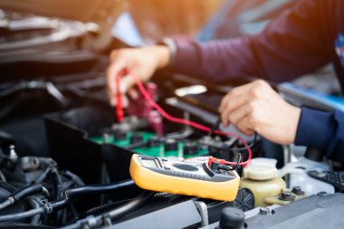 Bir tamirci bir araba motoru üzerinde çalışıyor. Pili kontrol etmek için çoklu metre kullanıyor..