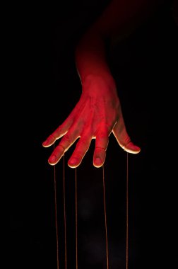 Siyah arka planda her parmağında ipler olan bir kuklacı eli..