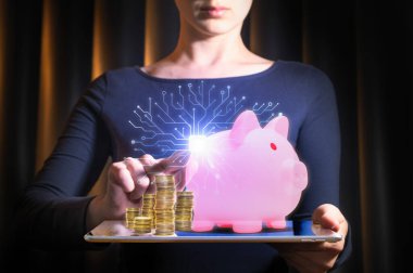 Sanal domuz kumbarası ve bozuk paralarla tablet üzerinde finansal uygulama kullanan genç bir kadın. Modern mobil bankacılık, dijital tasarruflar, fintech ve nakitsiz ödeme kavramı.