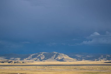 Peru And Dağları 'nda gün batımı. Mavi gökyüzü ve gri bulutlar. Tepeler, günbatımı güneşinin ışınlarıyla sarıya bürünüyor.