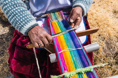 Zavallı yerli kadın sanatkar mavi maskeli ve tipik atadan kalma kostümlü. And Dağları 'nda güneşli bir günde covid-19 salgınında örgü örüyor.