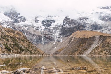 Peru cusco 'nun And Dağları' ndaki Humantay gölünde karla kaplı bulutlarla çevrili dağlar.