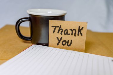 Geri dönüştürülmüş bir karton kutuya yazılan ve arka planda siyah bir fincan kahve olan teşekkür ederim.