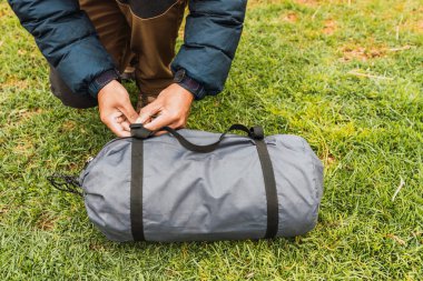 Adamın elleri, And Dağları 'nın doğal ışıklarıyla aydınlanmış yeşil çimenlerin üzerinde gri bir çadır çantası açıyor.