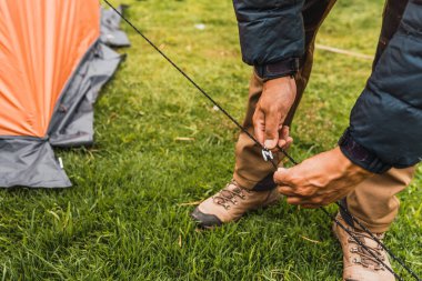 Adamın elleri, And Dağları 'nın doğal ışıklarıyla aydınlanan yeşil çimlerin üzerine turuncu bir çadır kuruyor.