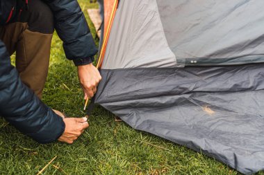 Adamın elleri, And Dağları 'nın doğal ışıklarıyla aydınlanan yeşil çimlerin üzerine turuncu bir çadır kuruyor.