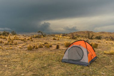 Andes sıradağlarındaki turuncu dağlık çadır fırtına bulutları ve ağaçlarla çevrili.