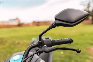 Güneşli bir günde yeşil arka planda dikiz aynalı siyah motosiklet gidonu