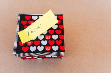 Teşekkür notu, kırmızı ve beyaz kalpli bir hediye kutusunun arka planına sahip mavi kalemle yazılmış.